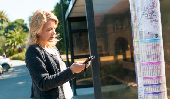 woman by transit stop looking on cell phone